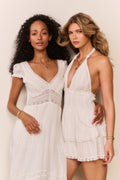 Two women wearing white dresses against a plain background