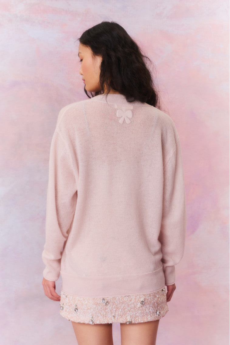 Button-down sweater with intricate ribbed details and tiny loops on them. The back features a bow applique at the neck and faux shell buttons with a custom LoveShackFancy bow on them that give off a shimmering pearlescent effect.