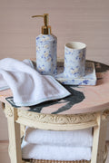 Bathroom set with floral soap dispenser, cup, and towel on a decorative table.