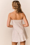 Woman wearing a white lace-trimmed and small floral print slip dress against a beige background