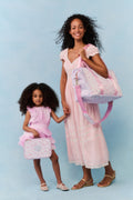 Two women, one adult and one child, holding matching pink bags against a light blue background.