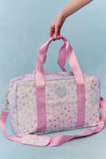 Pink floral patterned bag with heart design held by a hand against a light blue background