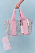 Clear floral print tote bag with pink straps and matching pouch on a light blue background