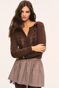 Brown cropped cable-knit cardigan featuring black bow details at the shoulders, black ribbon laced vertically down the front, and buttoned knit placket, styled closed