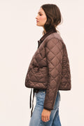 Side view of brown quilted jacket with dark brown corduroy collar and corduroy trim, snap button front, and front pockets with velvet bow trim
