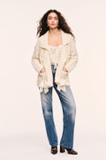Windel cardigan in ivory textured knit, open front with shawl collar, ribbon laced through the front, and ribbon bows on the pockets. Styled with jeans and heels.