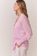 Pink cardigan worn by a woman in pink and white patterned pants on a plain background