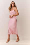 Woman wearing a pink satin cami and matching skirt with thin straps and bow detail on a plain background