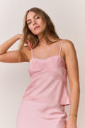 Woman wearing a pink satin slip cami and matching skirt against a plain background