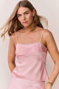Woman wearing a pink satin slip cami and matching skirt against a plain background