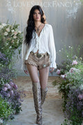 Woman in a stylish outfit with high boots and shorts, surrounded by flowers, with 'LOVE SHACK FANCY' branding.