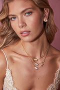 Woman wearing a gold necklace with gemstones against a pink background