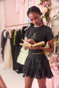 Woman in a black outfit reading a book in a room with clothing racks and floral decorations.