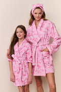 Two children wearing pink robes with a pattern on a beige background