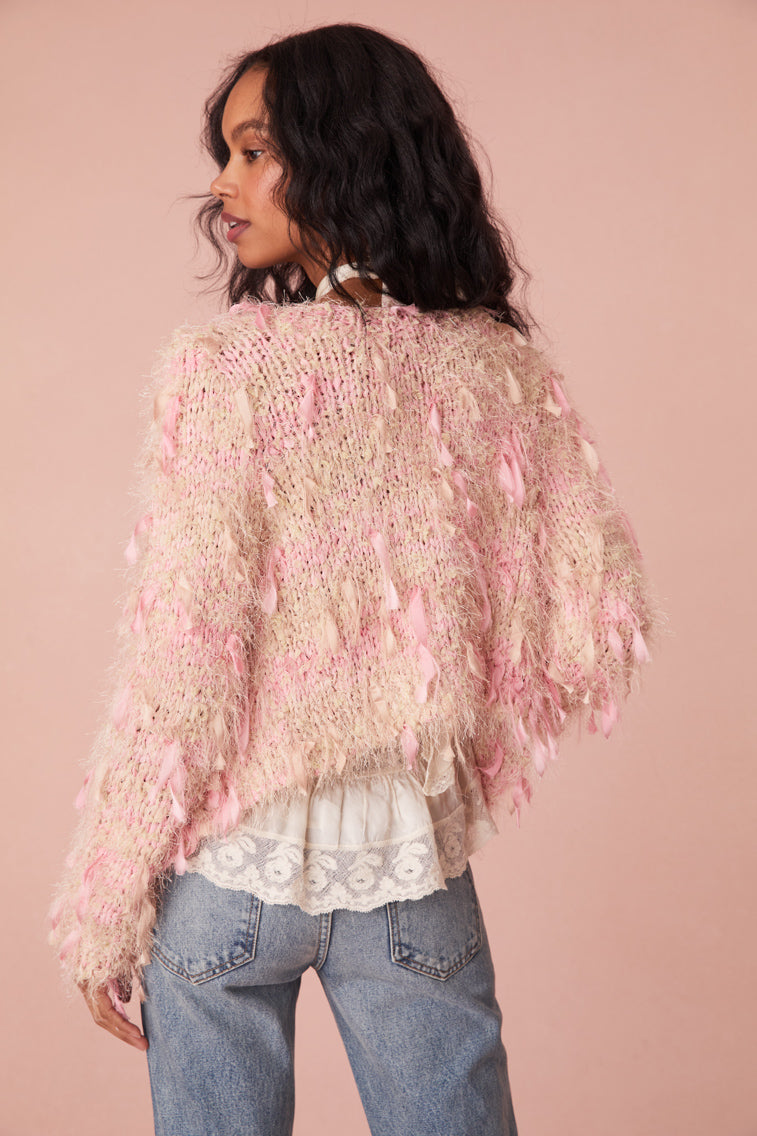 Eyelash boucle yarn cardigan with ribbons weaving in and out of the fabric to create a fringe effect. Features a LoveShackFancy faux shell button with a bow motif.