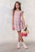 Young girl in a floral dress holding flowers against a plain background