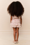 Young girl wearing a floral dress with ruffles from behind on a plain background