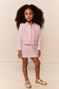 Young girl wearing a pink outfit with a matching jacket and skirt against a plain background