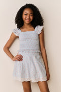 Young girl wearing Light blue floral pattered skirt with lace trim and matching shirt with ruffled details on a beige background