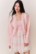 Woman wearing a pink cardigan with bow details and a pink and white lace trim skirt on a plain background