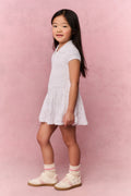 Young girl wearing a white t-shirt dress against a pink background