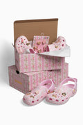 Pink clog shoes with gold hearts in a floral-patterned box on a white background