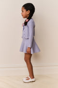 Young girl wearing a light blue cardigan and dress outfit against a plain background