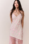 Woman wearing a pink floral dress with fringe hemline details on a plain background