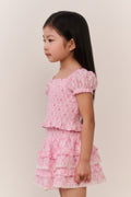 Young girl wearing a pink patterned ruffled top and matching skirt against a plain background