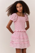 Young girl wearing a pink bow pattern top and matching ruffle skirt against a plain background