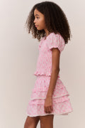 Young girl wearing a pink bow pattern top and matching ruffle skirt against a plain background