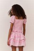 Young girl wearing a pink bow patterned ruffle top with matching skirt with ruffled layers on a plain background