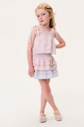 Young girl wearing a pink sleeveless top and matching skirt with ruffled layers on a white background