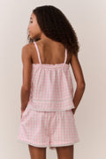 Young girl wearing a matching pink checkered sleeveless and shorts outfit against a plain background