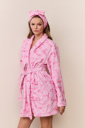 Woman wearing a pink robe with kiss print pattern and matching headband on a beige background