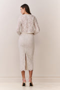 Woman wearing a white lace jacket and skirt outfit on a plain background