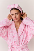 Woman wearing a pink bow print robe and headband against a light background