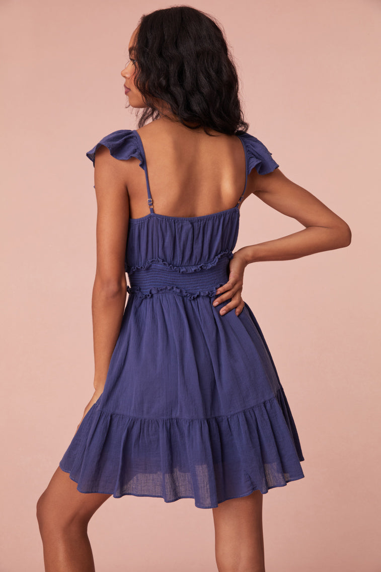 Mini dress featuring short flutter sleeves with cascading ruffles and elastication, a v-neckline, a smocked bodice with ruffles for a flattering silhouette, and a beautiful flouncy skirt.