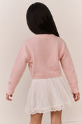 Young Girl wearing a pink sweater and white skirt lace against a plain background