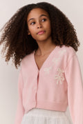 Tween wearing a pink sweater and white lace skirt on a plain background