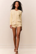Woman wearing a light yellow textured cardigan and shorts set against a plain background