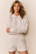 Woman wearing a white outfit with lace eyelet details on a beige background