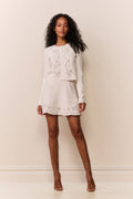 Woman wearing white eyelet trim mini skirt and matching cardigan