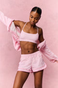 Woman wearing a pink gingham sports bra and shorts outfit against a pink background
