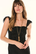 Woman wearing a black dress with lace sleeves and a long necklace on a white background