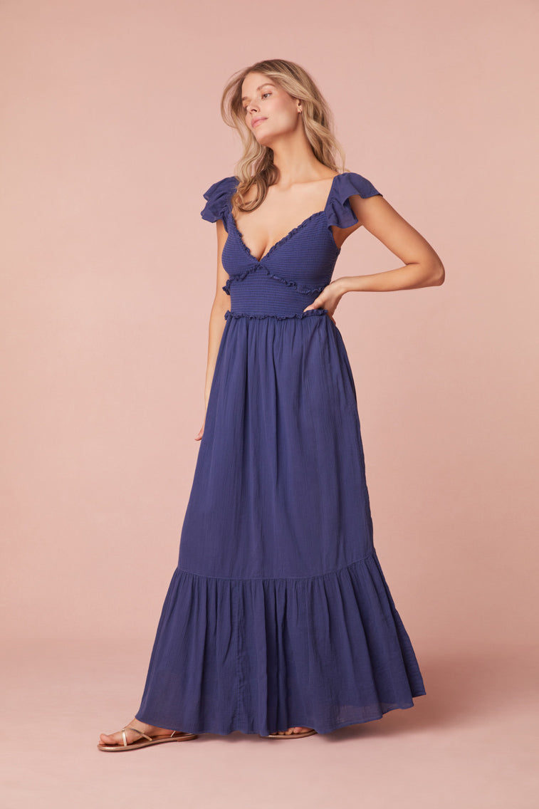 Maxi dress featuring short flutter sleeves with cascading ruffles and elastication for comfort, a v-neckline, a smocked bodice with ruffles, and a flouncy skirt.