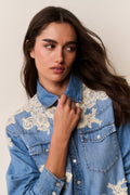 Woman wearing Blue denim shirt with floral lace embroidery on a beige background