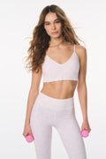 Woman wearing a white sports bra and leggings set with pink dumbbells on a white background