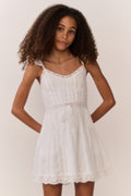 Tween girl wearing a white lace sleeveless dress against a plain background