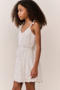 Tween girl wearing a white lace sleeveless dress against a plain background